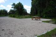 This is picture of campsite #79 from the back of the site looking toward the road.  Site has 50amp electric, water and sewage hook-ups.  This is a sunny site with stone foundation and vegetation on sides.  There is a separate section to the side with the picnic table, cooking grill and ground campfire ring.