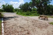 This is picture of campsite #80 from the back of the site looking toward the road.  Site has 50amp electric, water and sewage hook-ups.  This is a sunny site with stone foundation and vegetation on sides.  There is a separate section to the side with the picnic table, cooking grill and ground campfire ring.