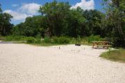 This is picture of campsite #82 from the back of the site looking toward the road.  Site has 50amp electric, water and sewage hook-ups.  This is a sunny site with stone foundation and vegetation on sides.  There is a separate section to the side with the picnic table, cooking grill and ground campfire ring.