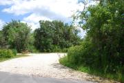 This picture of campsite #82 is looking from the road into the sunny site.  This site has 50 amp electric, water and sewer hook-ups. There is a stone foundation with vegetation on the sides.  There is also a separate area to the side with a picnic table, cooking grill and ground campfire ring.