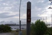 Sign post two situated to the right of an open campsite with a view of the lagoon in the distance. Electrical post and water spigot are located to the right of the post.
