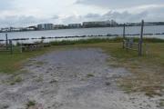 Extending down to the lagoon is a large open site. Gravel lies as a ground surface with grass on both sides and a Grand Lagoon view. Small native shrubs fill in the gaps under the tall pines by the water.