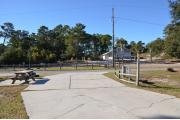 A large paved pull thru site that provides for ADA access is bordered by grass. In the distance are paved walkways leading to a bathhouse.