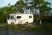 A grassy campsite is filled with a white travel trailer.