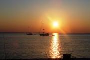 Two sailboats anchored in the calm waters of St. Joseph Bay as the sun rises over the water and their masts.