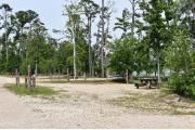 A picnic table and ground grill with electric and water in a campsite with view of lake.