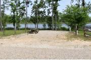 Campsite with picnic table and hook ups with view of lake through the trees.