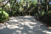 This campsite is tucked back in the shady hammock which provides cover most of the day. There is vegetation providing a boundary from neighboring sites. The ground cover is crushed shell, making a hard packed white surface.