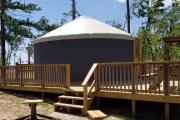 View of the inside of YURT showing a bunk futon with one full size bed on bottom and one single size bed on top, and a dining table.