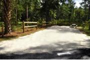 Campsite #1 at Wekiwa Springs State Park has a crushed shell surface and is surrounded by sections of split rail fence and trees creating partial shade on the site.  A picnic table and in-ground fire ring/grill are provided on the site along with water and 30amp electrical service.