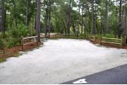 Campsite #4 at Wekiwa Springs State Park has a crushed shell surface and is surrounded by sections of split rail fence and trees creating partial shade on the site.  A picnic table and in-ground fire ring/grill are provided on the site along with water and 30amp electrical service.