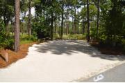 Campsite #6 at Wekiwa Springs State Park has a crushed shell surface and is surrounded by sections of split rail fence and Pine trees creating partial shade on the site.  A picnic table and in-ground fire ring/grill are provided on the site along with water and 30amp electrical service.