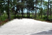 Campsite #11 at Wekiwa Springs State Park has a crushed shell surface and is surrounded by sections of split rail fence and trees creating partial shade on the site.  A picnic table and in-ground fire ring/grill are provided on the site along with water and 30amp electrical service.