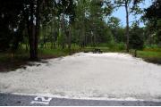 Campsite #12 at Wekiwa Springs State Park has a crushed shell surface and is surrounded by sections of split rail fence and trees creating partial shade on the site.  A picnic table and in-ground fire ring/grill are provided on the site along with water and 30amp electrical service.
