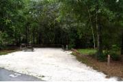 Campsite #13 at Wekiwa Springs State Park has a crushed shell surface and is surrounded by sections of split rail fence and trees creating partial shade on the site.  A picnic table and in-ground fire ring/grill are provided on the site along with water and 30amp electrical service.