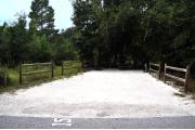 Campsite #15 at Wekiwa Springs State Park has a crushed shell surface and is surrounded by sections of split rail fence and trees creating partial shade on the site.  A picnic table and in-ground fire ring/grill are provided on the site along with water and 30amp electrical service.
