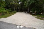 Campsite #16 at Wekiwa Springs State Park has a crushed shell surface and is surrounded by sections of split rail fence and trees creating partial shade on the site.  A picnic table and in-ground fire ring/grill are provided on the site along with water and 30amp electrical service.
