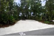 Campsite #24 at Wekiwa Springs State Park has a crushed shell surface and is surrounded by sections of split rail fence and trees creating partial shade on the site.  A picnic table and in-ground fire ring/grill are provided on the site along with water and 30amp electrical service.