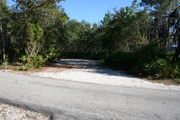 Photo is at the front of LOOP 1 #22 looking out towards back of site; gray campground road with green trees surrounding the site, also on the back of the site is 2 clothes line poles,  to the far right of site is water and electric hookups; far left of site is circular ground grill and picnic table.