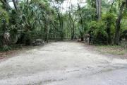 A September view of campsite #6 taken from the site entrance with tent/RV space in center of image, picnic table and fire ring on left hand side, and water and electrical hookups on right hand side.  Site is surrounded on three sides by a mixed oak, pine, and cabbage palm forest.