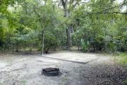 A September view of tent site #24, showing raised tent pad, with fire ring in foreground, and lantern post for your lantern.   Water and electrical hookups are a short distance away.  Site is surrounded on three sides by a mixed oak, pine, and cabbage palm forest.