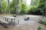 A September view of tent site #27, showing raised tent pad, fire ring, picnic table and lantern post.  Water and electrical hookups are a short distance away.  Site is surrounded on three sides by a mixed oak, pine, and cabbage palm forest.