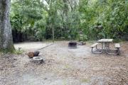 A September view of tent site #27, showing raised tent pad, fire ring, picnic table and lantern post.  Water and electrical hookups are a short distance away.  Site is surrounded on three sides by a mixed oak, pine, and cabbage palm forest.