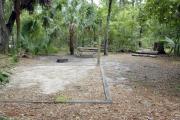 A September view of tent site #29, showing raised tent pad, fire ring, picnic table and lantern post.  Water and electrical hookups are a short distance away.  Site is surrounded on three sides by a mixed oak, pine, and cabbage palm forest.