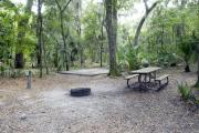 A September view of tent site #21, showing raised tent pad, with fire ring in foreground, picnic table, electrical hookup, and lantern post for your lantern. Water hookup is a short distance away.  Site is surrounded on three sides by a mixed oak, pine, and cabbage palm forest.