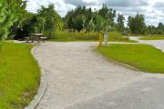 A 65 feet long gravel pull through campsite with vegetation giving privacy to the left. The sitting area is also located on the left and has a wooden picnic table and a cast-iron fire circle. Water and electric hook-ups are on the right hand side of the site.