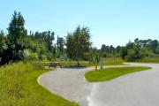A 75 feet long gravel pull through campsite with vegetation giving privacy to the left. The sitting area is also located to the left, opposite from the water and electric hookups. It has a wooden picnic table and a cast-iron fire circle.