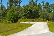 A 50 feet long gravel back up campsite with lush vegetation in the background. The sitting area is located to the left and has a wooden picnic table and a cast-iron fire circle. Water and electric hook-ups are on the right hand side of the site.