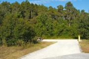 A 55 feet long gravel back up campsite with lush vegetation behind and to the sides of the site. The sitting area is located to the left and has a wooden picnic table and a cast-iron fire circle. Water and electric hook-ups are on the right hand side of the site.