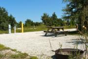 A fire circle and a picnic table in the foreground and the neighboring campsite across the road.