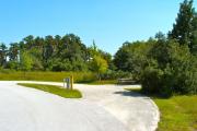 A 55 feet long gravel pull through campsite with vegetation giving privacy to the sitting area on the right, that has a wooden picnic table and a cast-iron fire circle. Water and electric hook-ups are on the left hand side of the site.