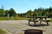 A fire circle and a picnic table in the foreground with the neighboring campsite across the road.