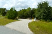 A 60 feet long gravel back up campsite with lush vegetation behind the site. The sitting area is located to the left and has a wooden picnic table and a cast-iron fire circle. Water and electric hook-ups are on the right hand side of the site.