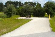 A 45 feet long gravel back up campsite with trees giving some privacy to the sitting area from the road leading into the campground. The sitting area is located to the left and has a wooden picnic table and a cast-iron fire circle. Water and electric hook-ups are on the right hand side of the site.