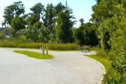 A 40 feet long gravel pull through campsite with vegetation giving some privacy to the right. The sitting area is also located to the right and has a wooden picnic table and a cast-iron fire circle. Water and electric hook-ups are on the left hand side of the site.