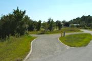 A 70 feet long gravel pull through campsite with vegetation giving some privacy to the left. The sitting area is also located to the left and has a wooden picnic table and a cast-iron fire circle. Water and electric hook-ups are on the right hand side of the site.