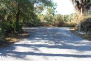 Looking into site from campground road; water spigot and electrical hook up on left; picnic table on right; site is paved