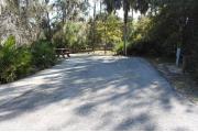 Looking into site from campground road; picnic table and standing grill are to the rear and left of the site; water spigot and electrical hook up on the right; site is paved