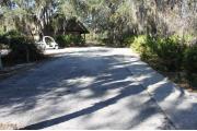 Looking out of site toward campground road;water spigot and electrical hook up are on the left; picnic table and standing grill are on the right; site is paved and a sidewalk leads to the bath house