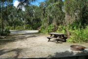 Looking toward campground road; water spigot and electrical hook up on left; picnic table and fire ring on left; site mostly sunny in afternoon