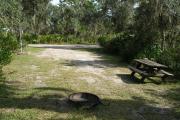 Looking out of site to campground road; fire ring in rear of site; picnic table on right; site partially shaded in afternoon