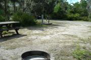Looking out of site toward campground road; picnic table, water spigot and electrical hook up on left; fire ring on left; site mostly sunny in afternoon