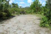 Looking into site from campground road; water spigot and electrical hook up on right; picnic table and fire ring on left; site mixture of grass and sand