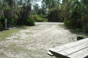 Looking out of site toward campground road; fire ring and picnic table on right; water spigot and electrical on left; site mixture of grass and sand,