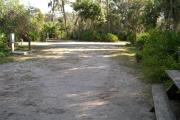 Looking out of site toward campground road; fire ring and picnic table on right; water spigot and electrical on left; site mixture of grass and sand