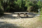 Looking into site from campground road; water spigot and electrical hook up on right; picnic table and fire ring on right; site mixture of grass and sand